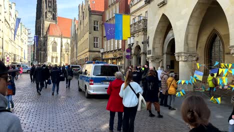 Gruppe-Von-Demonstranten,-Die-Gegen-Den-Krieg-Der-Ukraine-Gegen-Russland-Und-Putin-Demonstrieren---Schöne-Alte-Deutsche-Stadt-An-Einem-Sonnigen-Tag---Ukraine-Und-Europaflagge---Schwenk
