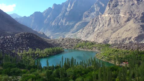 Aerial-view-of-turquoise-blue-water-at-upper-kachura-lake-surrounded-by-forest-in-skardu-pakistan-on-a-sunny-day-with-a-beautiful-large-mountain-range-in-the-distance