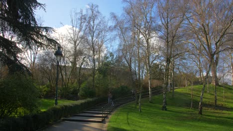 Vista-Del-Hermoso-Y-Relajante-Jardín-Verde-Y-Un-Camino-Cementado-Con-Escaleras-Que-Conducen-A-La-Carretera-Del-Parc-Montsouris,-Un-Jardín-Público-Ubicado-En-El-Barrio-De-Porte-D&#39;orleans-En-París,-Francia