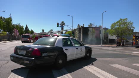 Polizeiauto-Und-Feuerwehrleute-Vor-Einem-Gebäudebrand-Im-Sonnigen-Los-Angeles,-USA