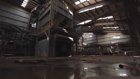 Slider-Footage-of-Machinery-in-an-Abandoned-Brick-Factory-with-a-Puddle-in-the-Foreground,-Shale-Storage,-Graffiti,-Decay,-Conveyor-Belts