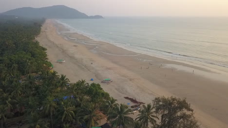Aerial-flyover-of-tropical-palm-lined-misty-Agonda-Beach-in-Goa,-India