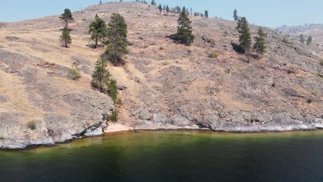 A-steep,-rocky-cliff-falling-into-Okanagan-lake-with-one-lonely-boat-anchoring-near-the-shore