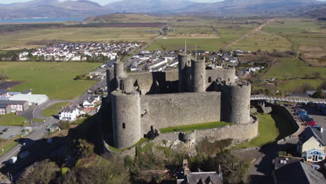 An-aerial-view-of-Harlech-Castle-on-a-sunny-day,-flying-left-to-right-around-the-castle-while-zooming-out,-Gwynedd,-North-Wales,-UK