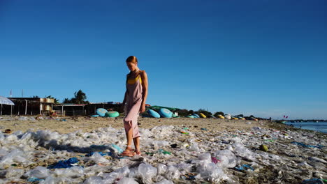 Tan-caucasian-blonde-girl-walking-alone-on-dirty-polluted-beach,-plastic-ocean-trash
