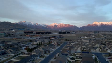 Idyllic-Community-below-snow-capped-mountains-at-sunset---sliding-aerial-hyper-lapse