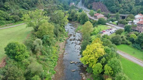 Flying-over-little-river-in-rural-hamlet-surrounded-by-trees-in-Spain