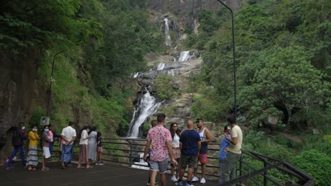 Slow-Motion-Shot-Of-Young-Guy-Holding-His-Drone-Walking-Towards-His-Friends-In-Front-Of-Ravana-Falls,-Sri-Lanka