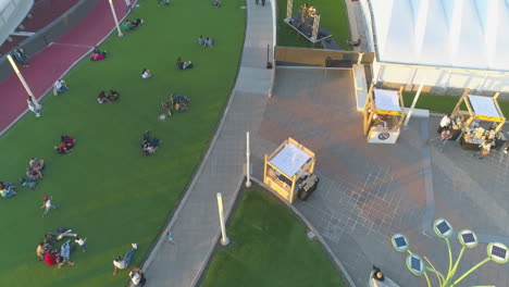 drone-aerial-video-of-outdoor-terrace,-chill-people-sitting-on-green-synthetic-grass,-chilling,-outside-costa-rica-shopping-center,-outdoor-concert,-luxury-sunset,-4k