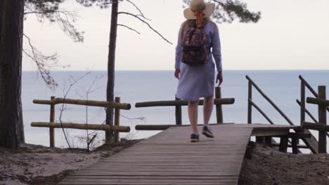 Beautiful-woman-walking-toward-Baltic-sea-coastline-on-wooden-pathway