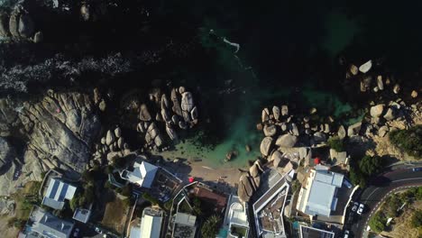 Birds-eye-drone-shot-of-Bakoven-beach-in-Camps-Bay,-Cape-Town---drone-is-descending-over-a-small-beach-cove