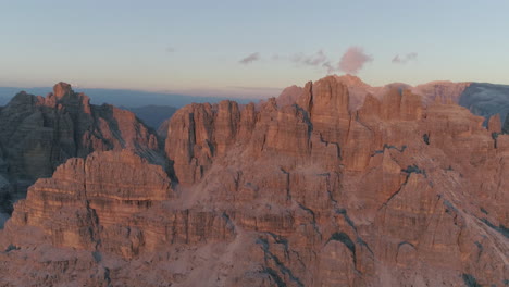 Rising-aerial-view-above-Tre-Cime-South-Tyrol-red-sunlit-rock-formation-mountain-range-shadowy-valley