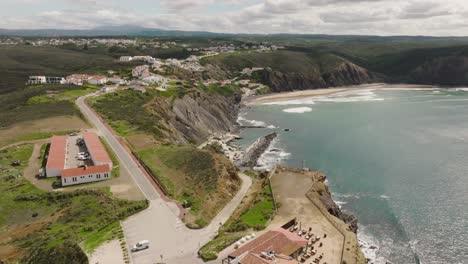 Long-aerial-shot-of-a-coastal-village-with-a-beautiful-secluded-beach-surrounded-by-cliffs