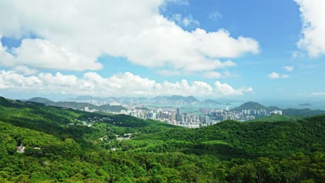 A-dynamic-ascending-aerial-footage-from-below-the-trees-revealing-the-beautiful-cityscape-of-Tseung-Kwan-O-New-town-in-Hong-Kong-surrounded-by-skyscrapers,-mountains-and-the-beautiful-seas