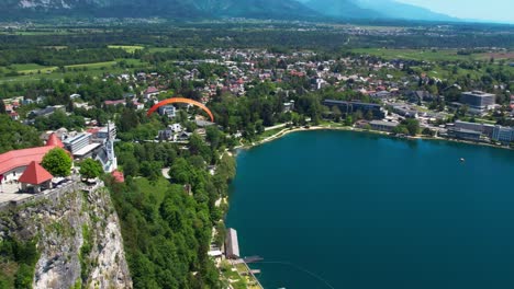 Luftaufnahme-über-Den-Bleder-See-In-Slowenien-Mit-Darüber-Schwebendem-Gleitschirm