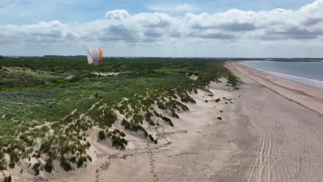 Lone-paraglider-drifting-along-lush-seaside-sand-dune-vegetation-on-dutch-beacheuro