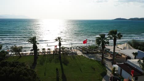 Aerial-landscape-of-Kusadasi-seaside-on-sunset,-Turkish-flag-in-background