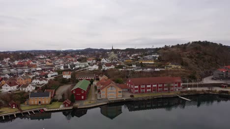 Kjellnabben-and-Bivika-in-Grimstad-with-city-center-and-church-in-background---Aerial-from-seaside-with-reflections-in-water-surface---Norway