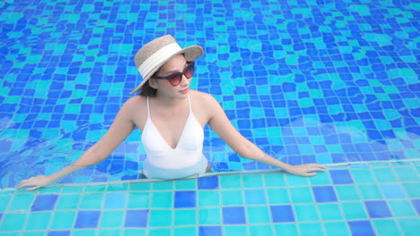 Elegante-Asiatische-Dame-Im-Blauen-Swimmingpool-Mit-Sommerhut,-Die-Den-Tropischen-Urlaub-Genießt,-Zeitlupe