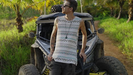 Male-Wearing-Sunglasses-Leaning-Against-Bonnet-Of-Dirt-Buggy-And-Folding-Arms