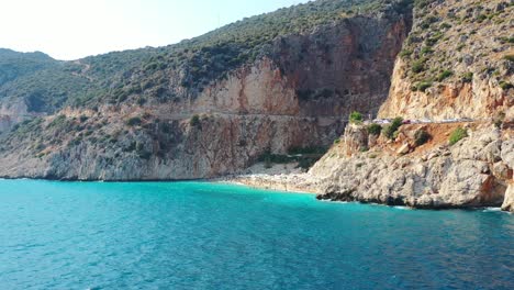 Aerial-drone-panning-in-at-Kaputas-Beach-in-Kas-Turkey-on-a-sunny-afternoon-day-during-summer-as-European-tourists-sun-bathe-surrounded-by-beautiful-blue-Mediterranean-Sea-and-Mountain-Cliffs