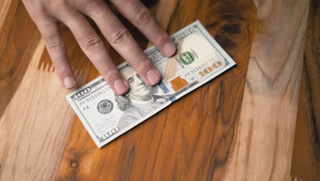 Sliding-one-hundred-dollar-bill-on-the-table-for-someone,-hands-only