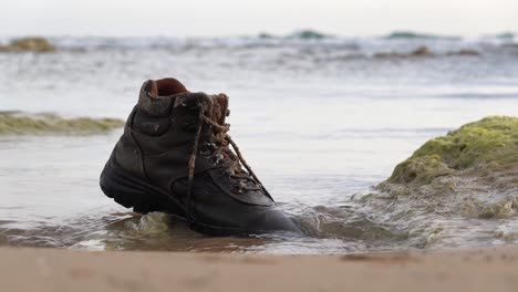 Abandoned-shoe-as-a-garbage-on-a-sangy-beach-in-Sicily,-Italy-with-slight-slow-motion-effect