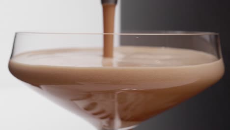 Close-up-shot-of-espresso-being-poured-into-a-martini-glass-with-a-half-black-and-half-white-background,-foamy-bubbles