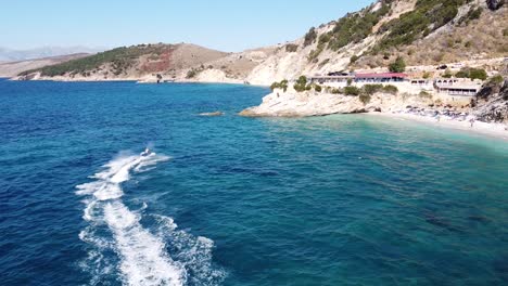 Fast-Jetski-Sails-across-Blue-Sea-at-Pulebardha-Beach,-Ksamil,-Albania---Aerial-Dolly