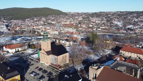 Kongsberg-church-ascending-aerial-view---Church-seen-in-middle-of-city-center-with-Numedalslagen-river-behind---Blue-sky-winter-Norway