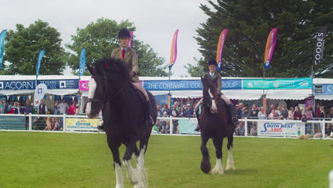 Die-Royal-Cornwall-Show-2022-Mit-Weiblichen-Jockeys-Auf-Großen-Shire-Pferden,-Die-Mit-Einem-Publikum-Im-Hintergrund-Vorbeiziehen-–-Zeitlupe