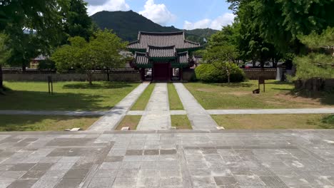 Tilt-up-shot-of-beautiful-old-korean-temple-in-surrounded-by-green-nature-with-trees-and-mountains-during-sunlight