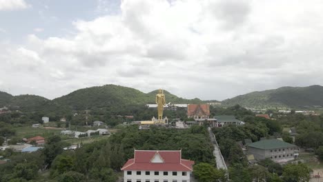 Drone-Flying-backwards-from-Golden-standing-Buddah-Statue-at-Wat-Khao-Noi-temple,-Hua-Hin