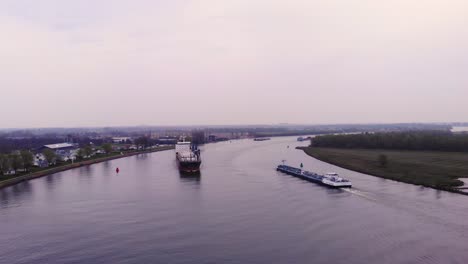 Aerial-View-of-Fortune-Cargo-Ship-Approaching-Along-Oude-Maas-On-Cloudy-Day-Passing-Another-Ship-On-River-Bend