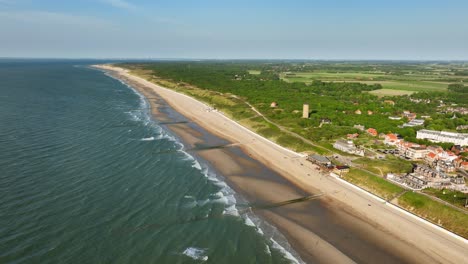 Aerial-shot-of-changing-tides-outside-a-picturesque-little-coastal-town-in-a-green,-rural-area,-on-a-beautiful-summer-day