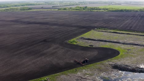 Aerial-shot-of-tractor-cultivating-large-unplanted-field