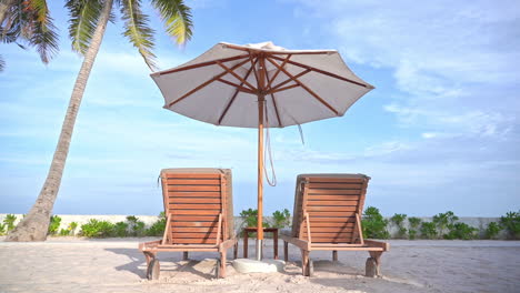 Empty-beach-deckchairs-under-Umbrella-against-blue-sky-next-to-tropical-Palm