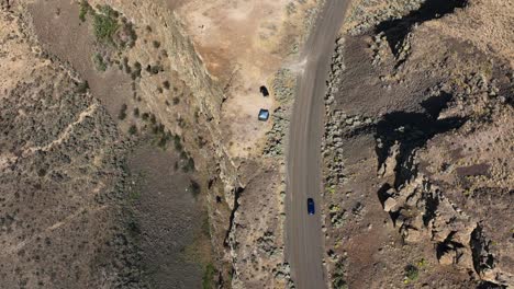 Top-down-aerial-shot-of-a-car-driving-through-Eastern-Washington's-desert-terrain