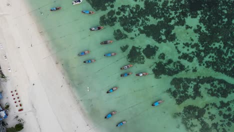 top-down-view-of-longtail-boats-docked-on-white-sand-beach-in-Koh-Lipe-Thailand,-aerial,-zoom-out,-camera-rotating