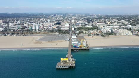 Turquoise-Beach-Waters-Sweeping-Along-Santa-Monica-Fishing-Pier-And-Amusement-Park-In-California,-US-With-Extensive-Cityscape-View