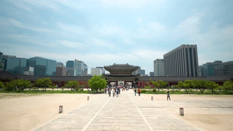 Heungnyemun-Gate-with-people-walking-far-away-and-Seoul-business-center-Buildings-and-Government-building-behind,-Gyeongbokgung-Palace