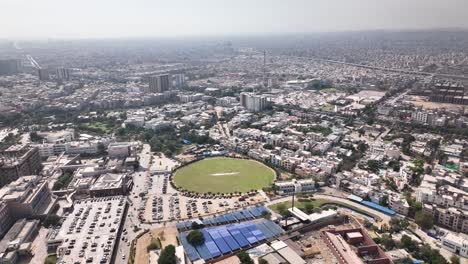 Toma-Aérea-De-La-Ciudad-De-Karachi-Llena-De-Edificios-Y-Casas-Y-Campo-De-Cricket-En-Medio-De-La-Ciudad