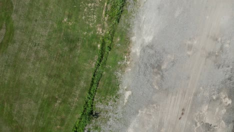 Green-trees-grass-and-plants-contrast-with-grey-construction-gravel-dirt,-aerial