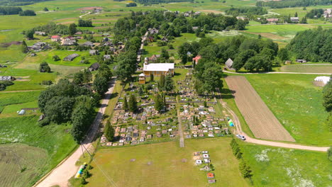Vista-Aérea-De-La-Iglesia-Católica-Y-El-Cementerio-En-Un-Pequeño-Pueblo-Rural-En-El-Campo-De-Lituania,-Disparo-De-Drones