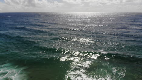 Luftaufnahme-Tiefblauer-Meereswellen,-Sonnenreflexion-Und-Wolken-Im-Hintergrund