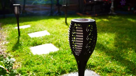 Solar-powered-stylish-modern-torch-lighting-on-sunlit-garden-lawn-grass