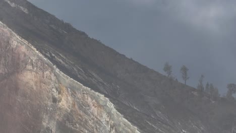 Sheer-steep-rock-wall-of-volcano-crater-with-light-clouds-from-sulfur-fumes,-aerial