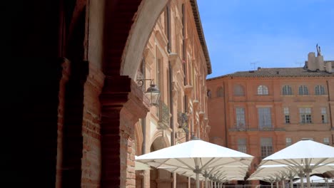 The-Montauban-town-square-with-parasol-umbrellas-and-architectural-brick-arches,-Dolly-right-reveal-shot