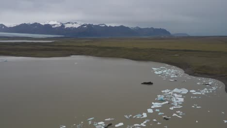 Glacier-in-Iceland-with-blue-ice-floating-in-water-and-mountain-view-with-drone-video-moving-forward