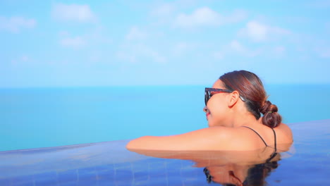 Woman-leaning-on-edge-of-infinity-swimming-pool-and-looking-to-the-sea